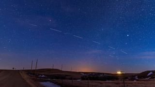 a series of white streaks parade across the night sky against the background of stars. 